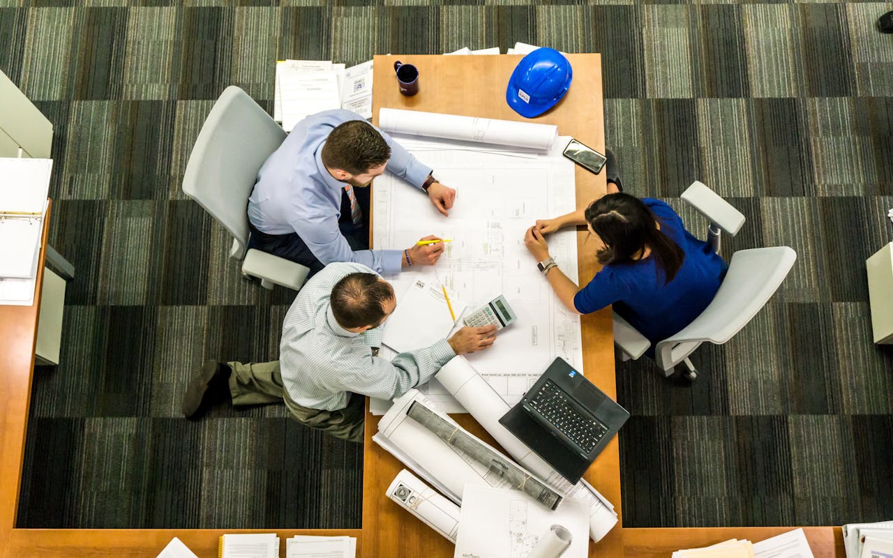 hero-img-01 Top view of a team working on construction plans in an office setting.
